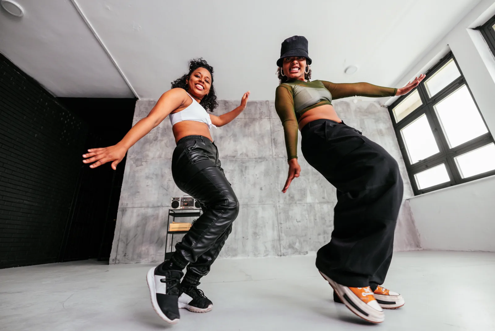 Two hip-hop dancers mid-pose in a concrete-walled urban dance studio.